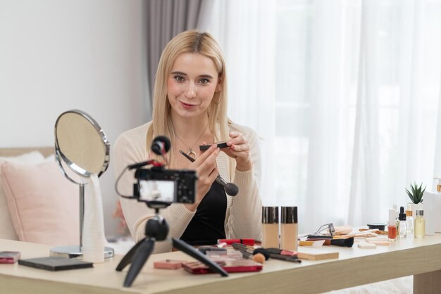 Młoda kobieta tworzy treści wideo z poradnikami kosmetycznymi i kosmetycznymi dla mediów społecznościowych Beauty blogger uśmiecha się do kamery, pokazując, jak dbać o urodę publiczności lub obserwatorom Blithe