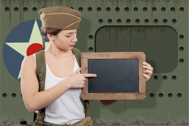 Zdjęcie młoda kobieta ubierająca w wwii wojskowym uniformu z nakrętka seansu pustym pustym chalkboard z kopii przestrzenią