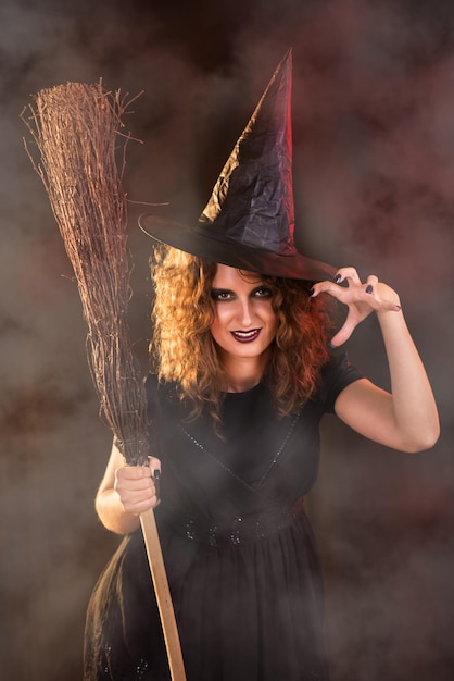 Młoda kobieta ubrana jak czarownica. Jest w ciemnym ubraniu i trzyma miotłę.
