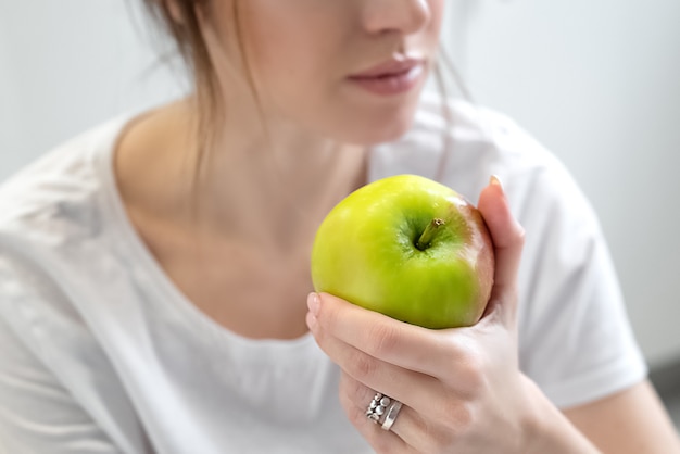 Młoda kobieta ubrana w białą koszulkę trzyma w ręku zielone dojrzałe jabłko. Dieta i zdrowe odżywianie