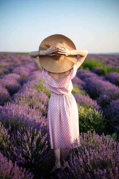 Młoda kobieta ubrana w długą sukienkę i słomkowy kapelusz stojąca na lawendowym polu