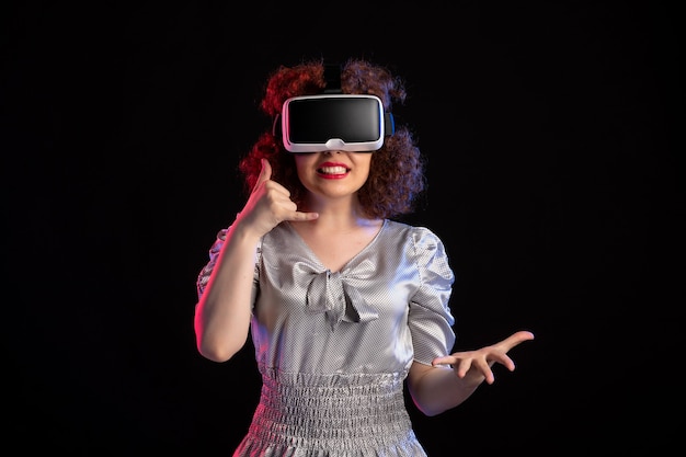 Młoda kobieta ubrana w zestaw słuchawkowy wirtualnej rzeczywistości na ciemnej powierzchni