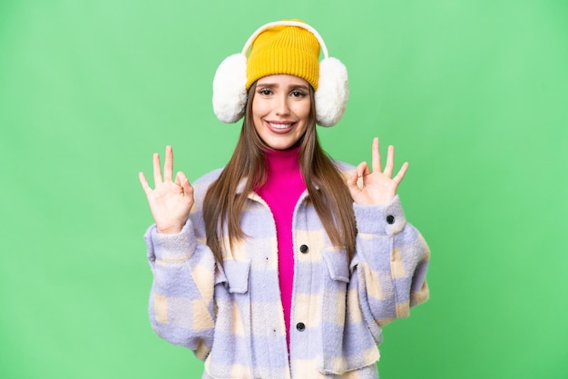 Młoda kobieta ubrana w zimowe mufki na odizolowanym tle klucza chrominancji, pokazująca znak ok palcami