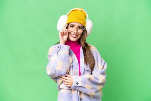 Młoda kobieta ubrana w zimowe mufki na odizolowanym tle z kluczem chrominancji w okularach i szczęśliwa