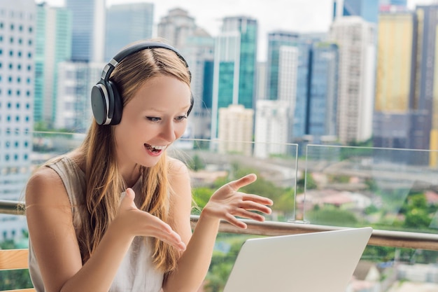 Młoda kobieta uczy języka obcego lub uczy się języka obcego przez Internet na swoim balkonie na tle wielkiego miasta Styl życia szkoły językowej online