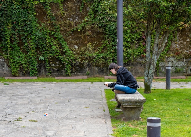 Młoda kobieta uniwersytecka czyta książkę siedząc na kamiennej ławce w przerwie otoczonej piękną zieloną trawą