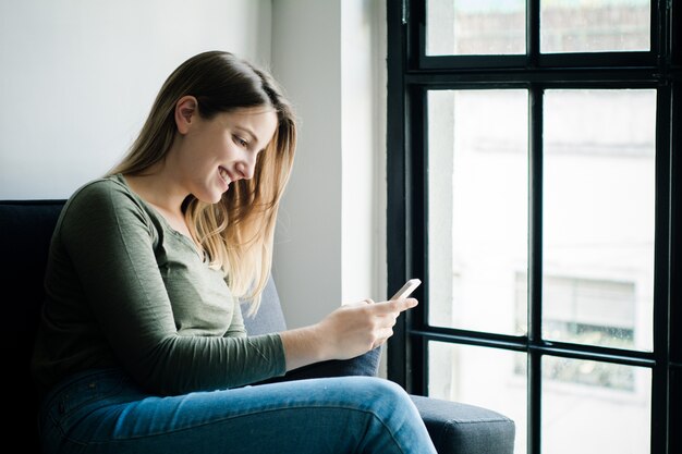 Młoda kobieta używa jej smartphone na kanapie