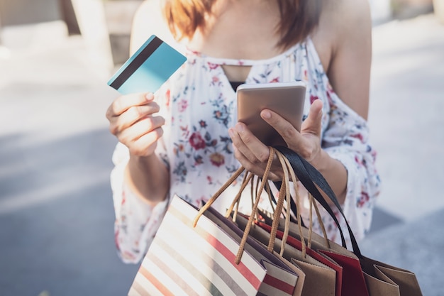 Zdjęcie młoda kobieta używa smartphone z torba na zakupy i kredytowa karta przy zakupy centrum handlowym na czarny piątek