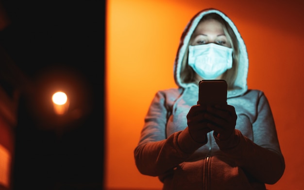 Młoda Kobieta Używa Telefon Komórkowego Plenerowego Podczas Gdy Będący Ubranym Zbawczego Twarzy Piżmo Podczas Coronavirus Wybuchu Przy Nighttime