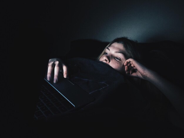 Zdjęcie młoda kobieta używająca laptopa leżąc na łóżku w ciemni