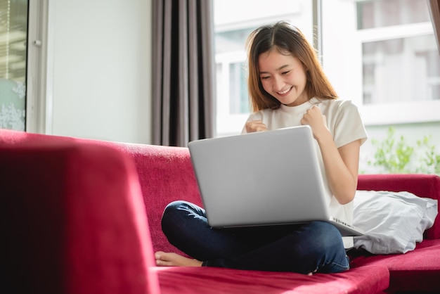 Młoda kobieta używająca laptopa siedząc w domu na kanapie