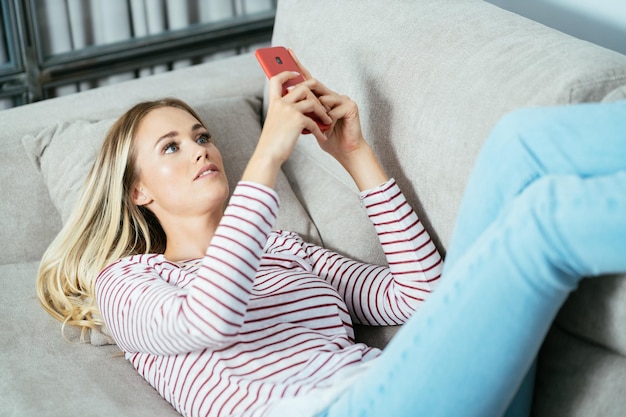 Zdjęcie młoda kobieta używająca smartfonu leżąc w domu na kanapie