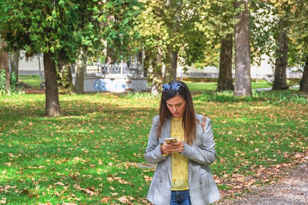 Młoda kobieta używająca telefonu komórkowego podczas spaceru po parku