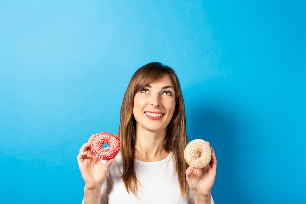 Młoda kobieta w białej koszulce trzyma pączki na białym tle