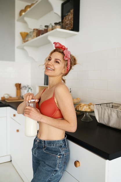 Młoda kobieta w bieliźnie otwiera butelkę z mlekiem i uśmiecha się do kuchni