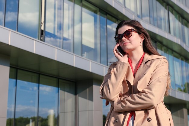 Młoda kobieta w biznesowym stroju rozmawia przez telefon w tle biurowca