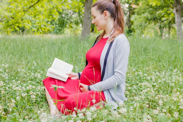 Młoda kobieta w ciąży czyta książkę w parku, siedząc na trawie Nieostrość