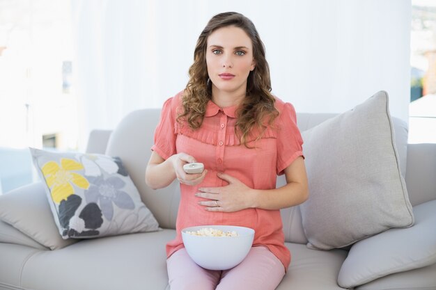 Młoda kobieta w ciąży oglądania telewizji siedzi na kanapie