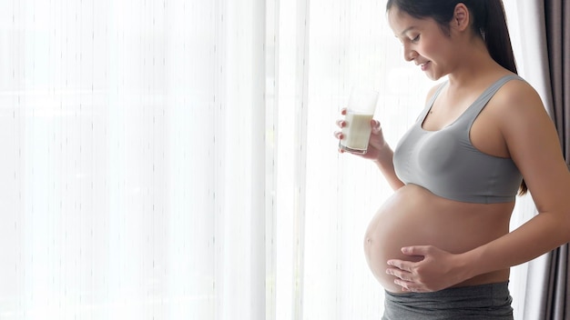 Młoda kobieta w ciąży pije mleko w domu opieka zdrowotna i opieka nad ciążą