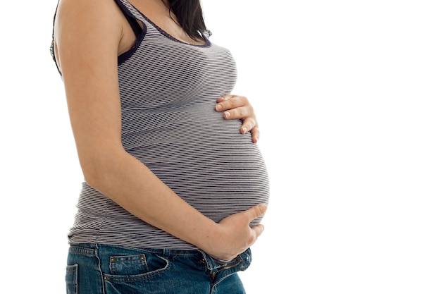 Młoda kobieta w ciąży pozowanie na białym tle na białej ścianie bez twarzy