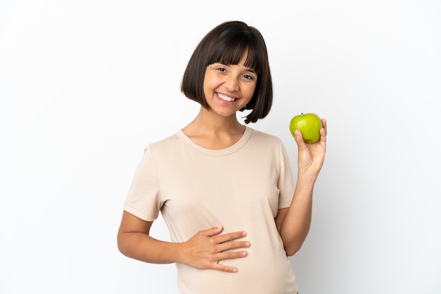 Młoda kobieta w ciąży rasy mieszanej na białym tle z jabłkiem i szczęśliwa