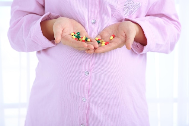 Młoda kobieta w ciąży trzymająca tabletki na jasnym tle