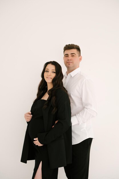 Młoda kobieta w ciąży z mężem w stylowych eleganckich czarnych ubraniach na jasnym tle