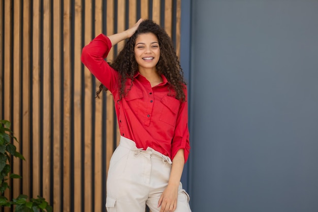 Młoda kobieta w czerwonej koszuli stojąca na szarej i drewnianej ścianie