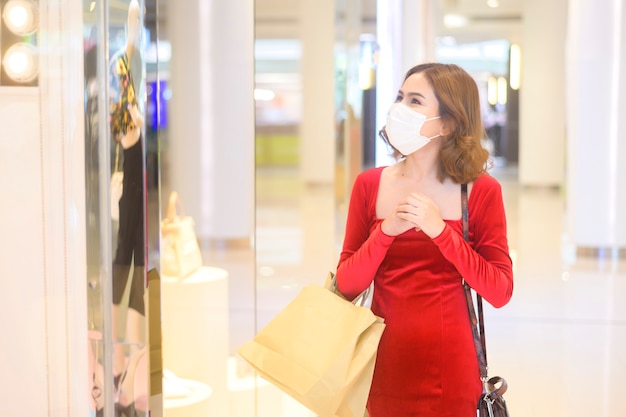 Młoda kobieta w czerwonej sukience nosząca maskę ochronną w centrum handlowym, robiąca zakupy w ramach koncepcji pandemii Covid-19.