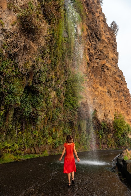 Młoda Kobieta W Czerwonej Sukience Patrząca Na Wodospad, Który Spada Na Drogę O Nazwie Anjos Waterfall Madeira