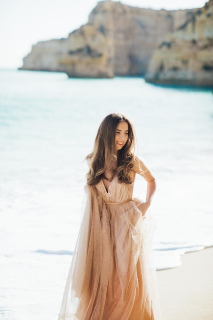 młoda kobieta w długiej sukni spaceru na plaży w pobliżu oceanu.