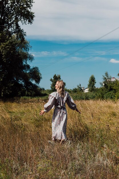 Młoda kobieta w długiej wiejskiej sukni stoi na polu plecami do przodu