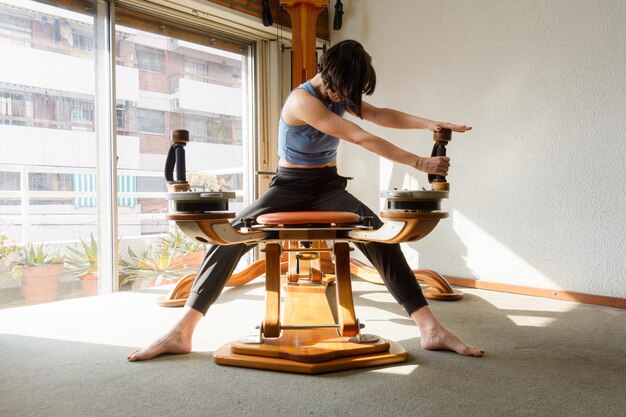Zdjęcie młoda kobieta w domu trenuje ramiona i ramiona obiema rękami w tym samym kierunku na maszynie do ćwiczeń