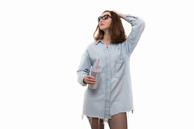 Młoda kobieta w dżinsowej koszuli i rajstopach pije koktajl ze szklanki