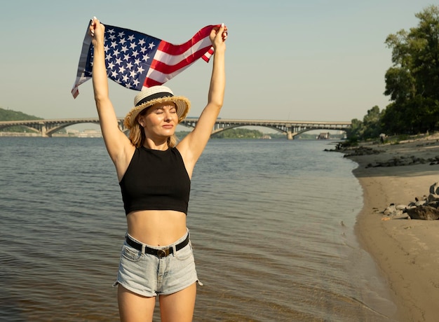 Młoda kobieta w dżinsowych szortach stoi nad wodą w mieście z flagą USA Święto Niepodległości