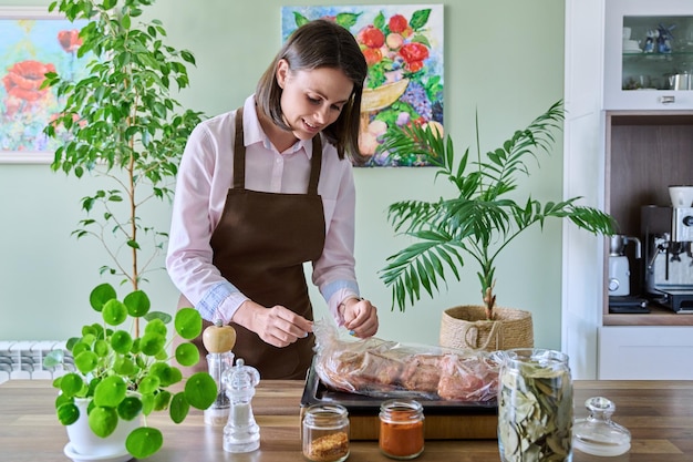 Młoda kobieta w fartuchu gotuje mięso w kuchni rękawa do pieczenia w domu