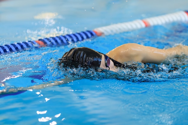 Młoda kobieta w gogle i czapka pływanie styl obrysu kraulem w niebieskim basenie krytym wyścigu.