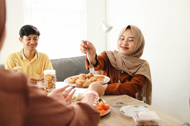 Zdjęcie młoda kobieta w hidżabie bierze ciasteczka z talerza podczas wspólnej kolacji iftar w domu