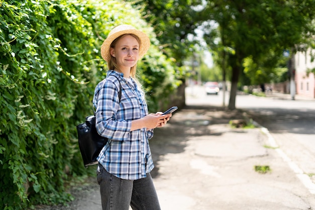 Młoda Kobieta W Kapeluszu I Koszuli Ze Smartfonem Podróżuje Spacerując Po Mieście Hipster Dziewczyna Przegląda Internet Na Telefonie Komórkowym Patrząc