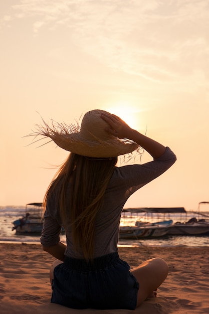Młoda kobieta w kapeluszu patrząca na zachód słońca w oceanie