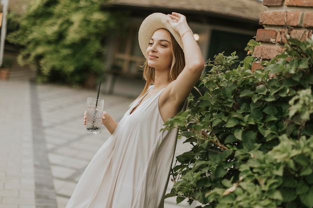 Młoda kobieta w kapeluszu pijąca zimną lemoniadę w ogrodzie kurortu