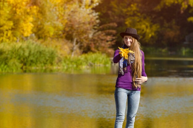 Młoda kobieta w kapeluszu stoi na molo. Jesienny słoneczny dzień. Widok z tyłu