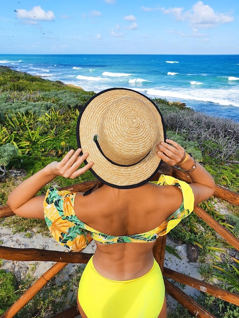 Zdjęcie młoda kobieta w kapeluszu stoi plecami i patrzy na ocean