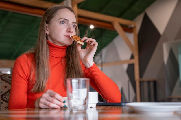 Młoda kobieta w kawiarni próbuje przekąskę Dziewczyna siedzi przy stołem w kawiarni i trzyma deser w jej ręce Zamyślona lub smutna kobieta