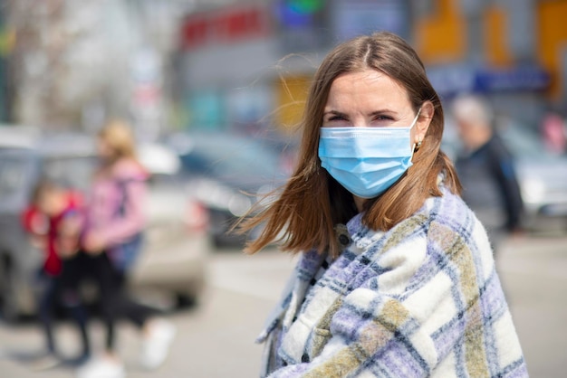 Młoda kobieta w masce medycznej stoi na parkingu w pobliżu sklepu spożywczego