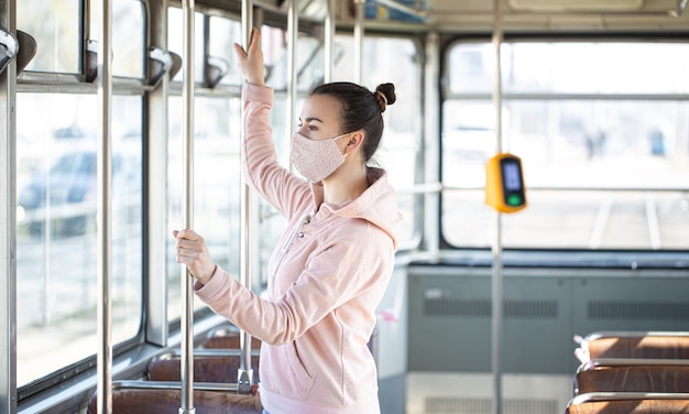 Młoda kobieta w masce stoi samotnie w transporcie publicznym podczas pandemii koronawirusa.