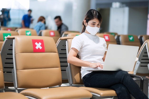 Młoda kobieta w masce twarzy za pomocą laptopa na lotnisku