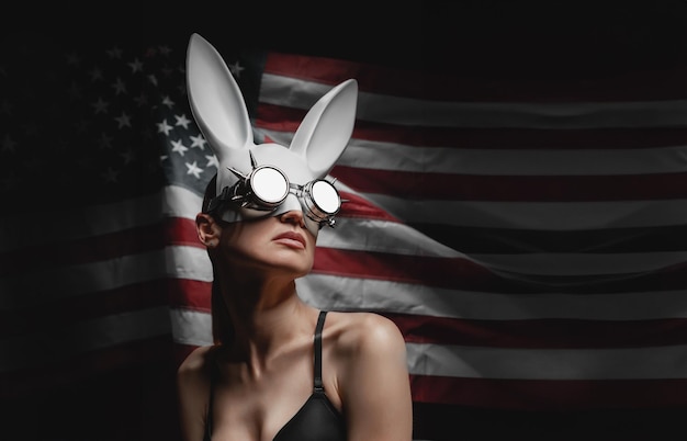 Młoda kobieta w masce zająca na tle amerykańskiej flagi w okularach steam punk
