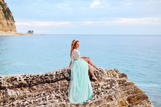 Młoda kobieta w miętowej sukience siedzi na dużym kamieniu na brzegu Morza Adriatyckiego