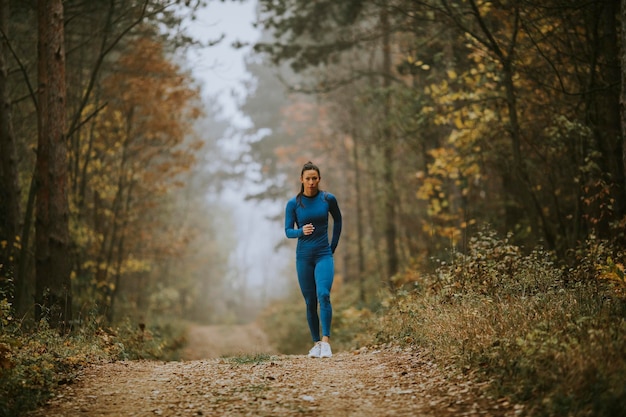 Młoda Kobieta W Niebieskim Dresie Biegnąca W Kierunku Kamery Na Leśnym Szlaku Jesienią